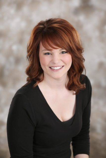 Professional woman with red hair and a black top smiles in front of a soft neutral backdrop during her personal branding portrait session with Mueller Photography in La Crosse, WI.