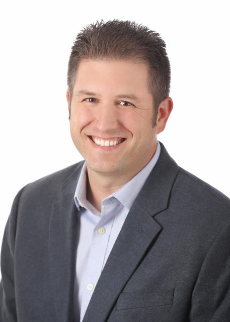 Professional man with short dark hair smiles in a gray blazer and light blue shirt against a clean white background during his personal branding session with Mueller Photography in La Crosse, WI.